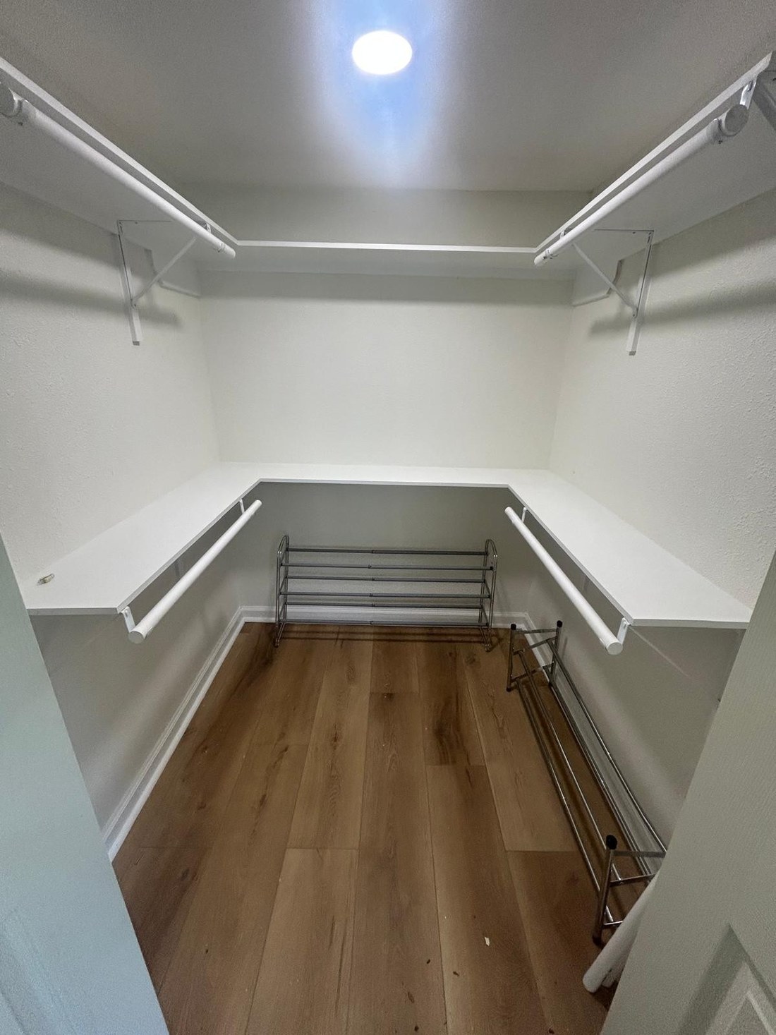 The same space converted into a walk-in closet with painted walls, white shelving and hanging rods, baseboards and wood plank flooring