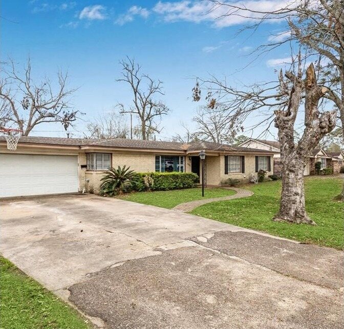 Tan brick ranch house with a white garage door before painting