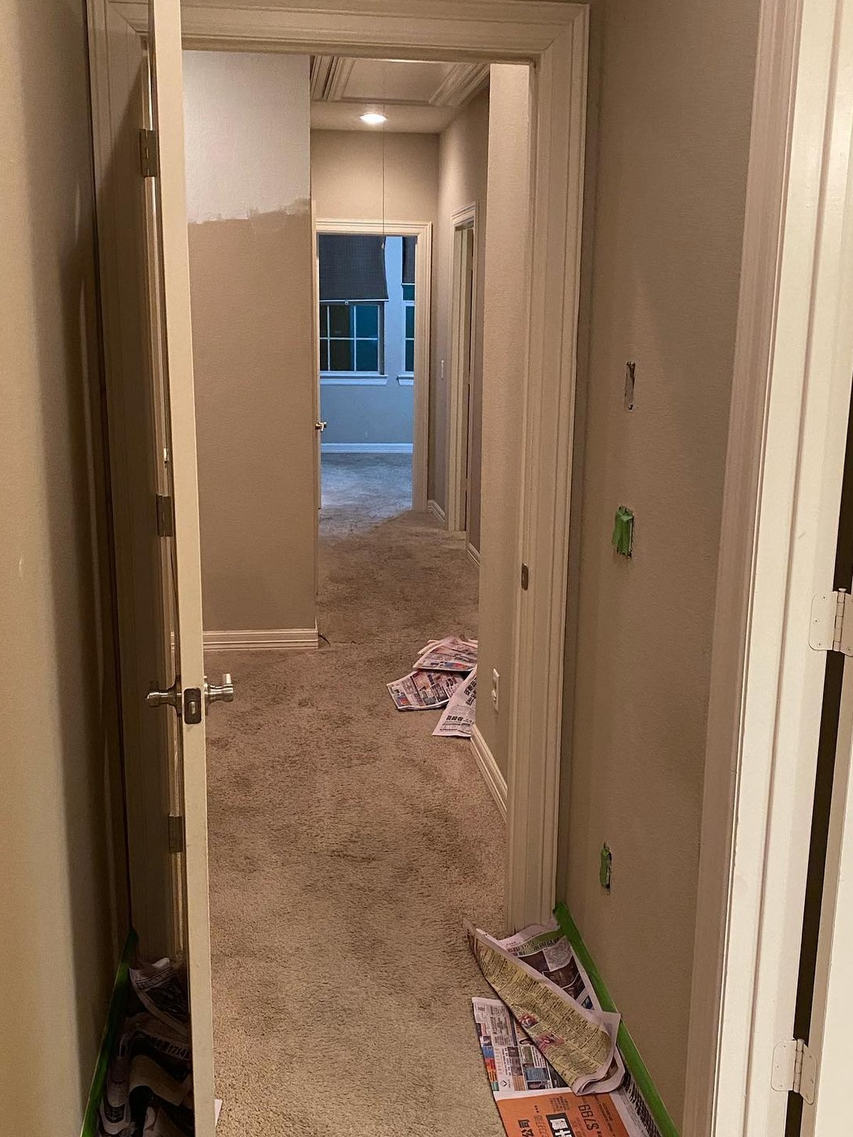 Hallway with tan walls, newspaper on the carpet and doors taped off
