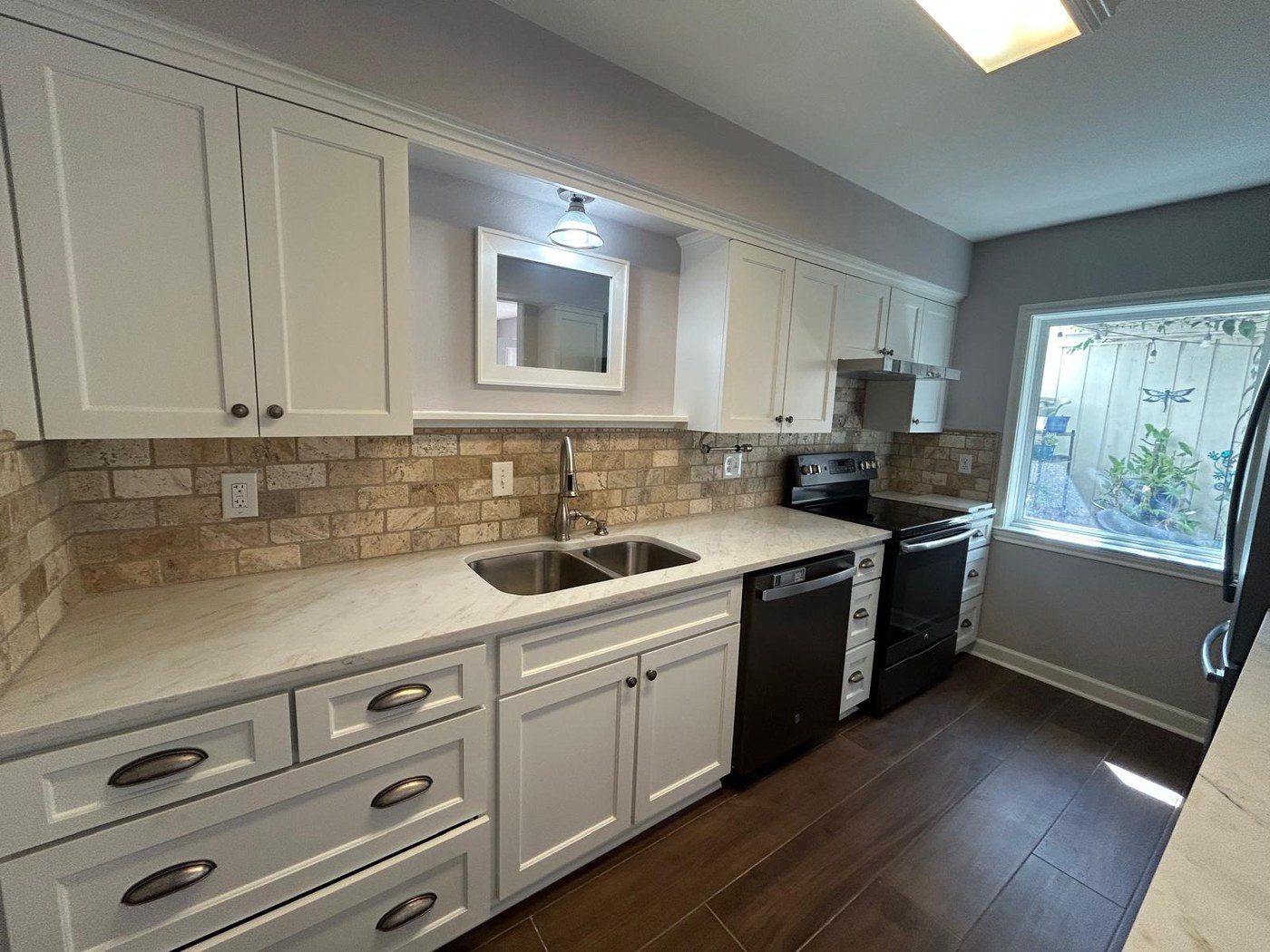 The same sink run with white quartz counters, refinished white cabinets and wood-look ceramic tile floor