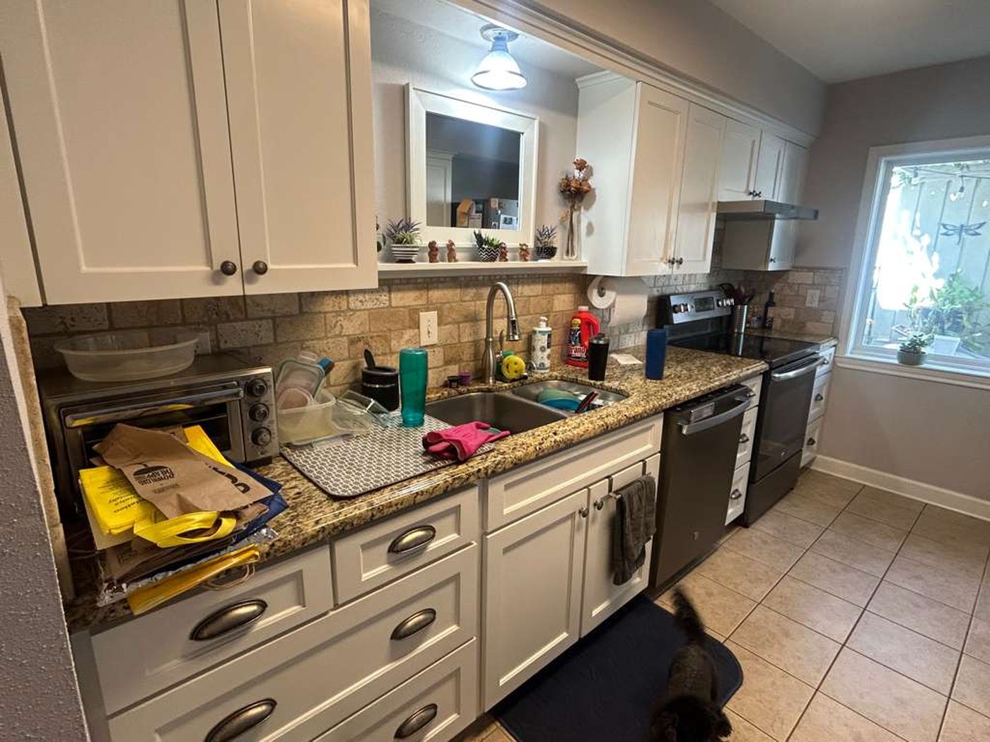 Kitchen sink run with beige granite counters, stone backsplash and cream tile floor