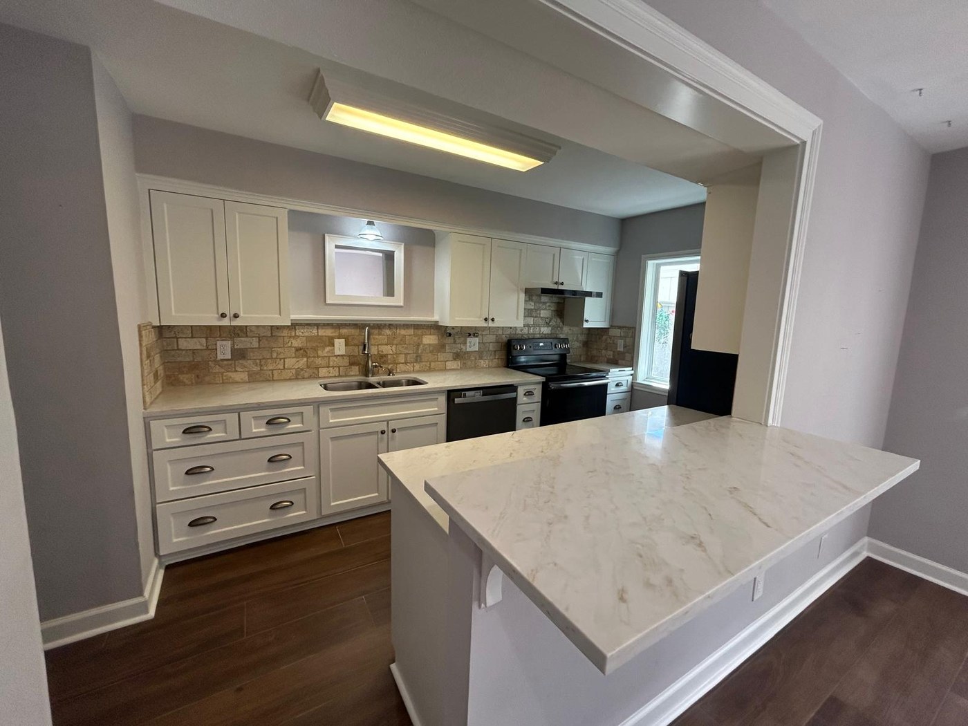 The same view with a white quartz island, refinished cabinets and new ceramic plank flooring