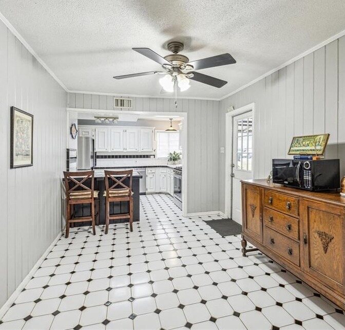 Breakfast area with pale paneling, a textured ceiling and dated cabinets beyond