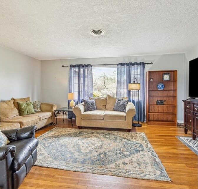 Living room with beige walls, a textured ceiling and worn wood floors